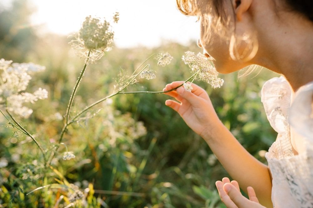 Adorable little girl wearing natural white dress with wildflower in green field