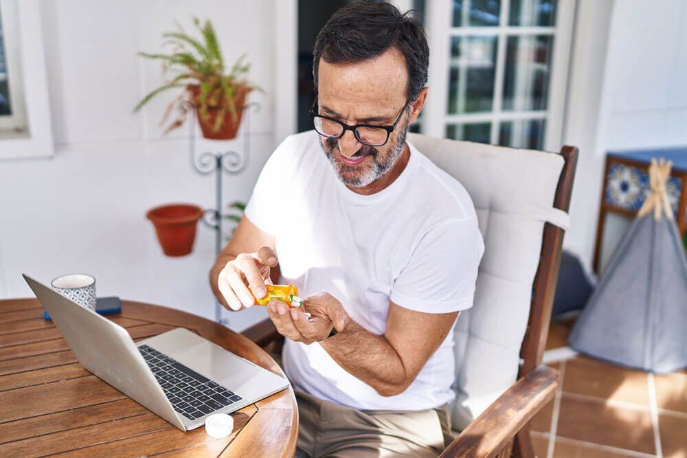 Middle age man using laptop taking pills at terrace home
