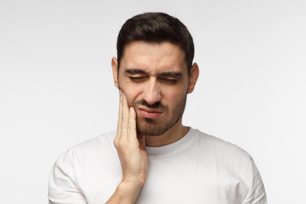 young man feeling pain, holding his cheek with hand