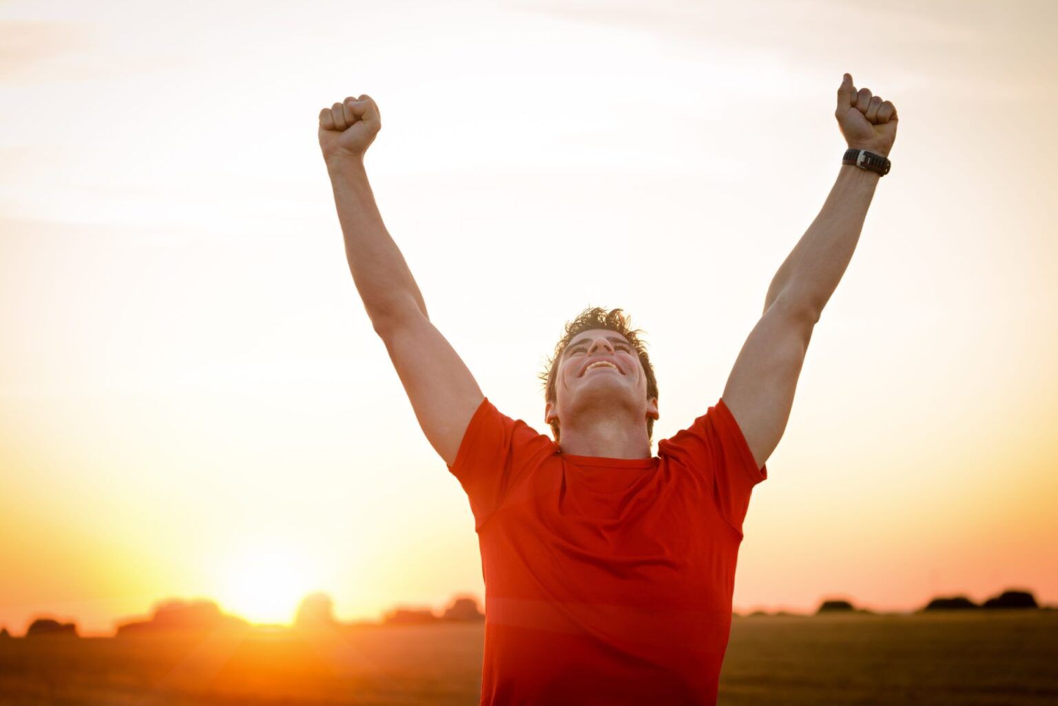 Successful man raising arms after cross track running on summer sunset