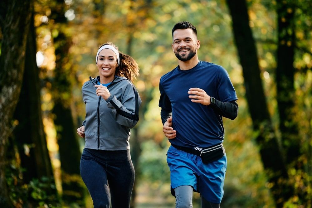 Happy athletic couple jogging during autumn day in the park