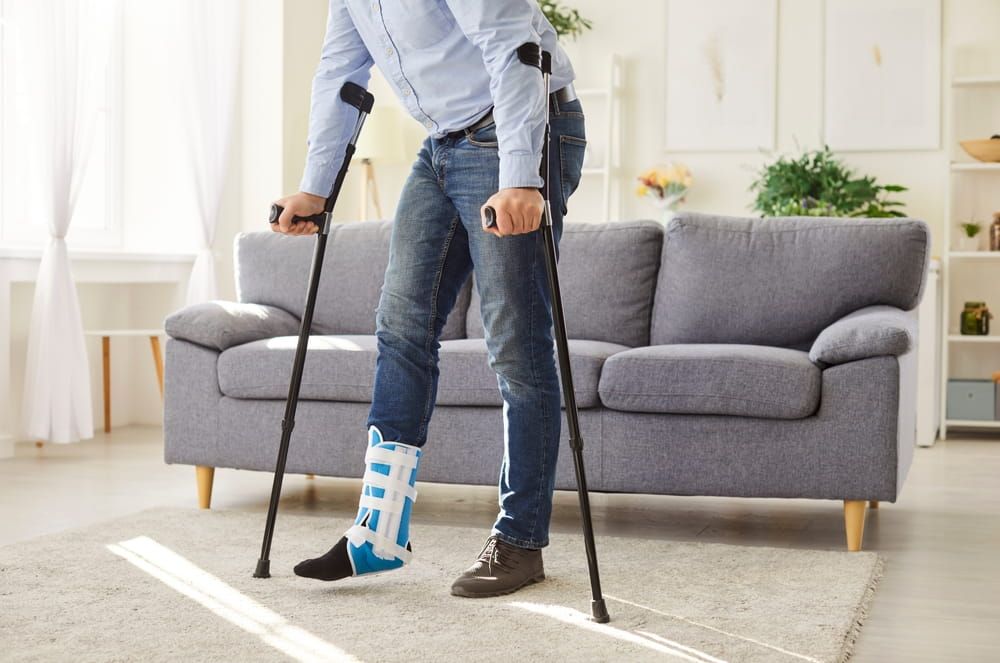 Man wearing sling on broken injured leg, rehabilitation after hurt, injury with foot pain at home