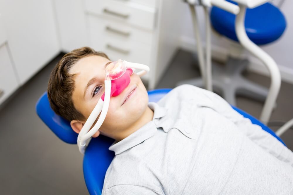 A little boy sits in a dentist's office wearing a nasal mask