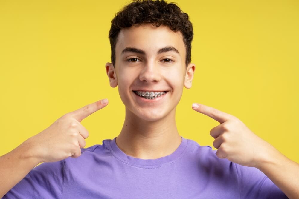 Smiling confident teenager pointing fingers on dental braces
