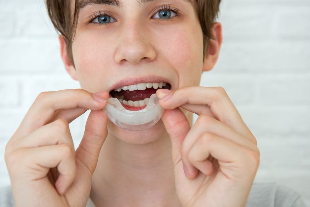 Positive teen boy holds mouth guards for her teeth.