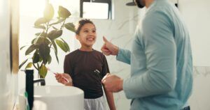 Child, father and brushing teeth with thumbs up in bathroom