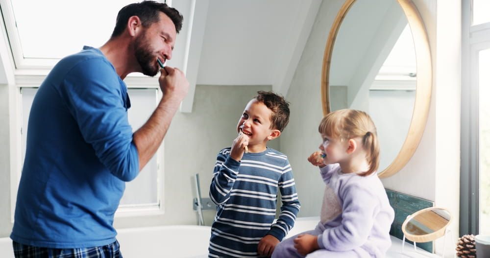 Father, bathroom and brushing teeth with children in home for morning routine, dental hygiene and oral health