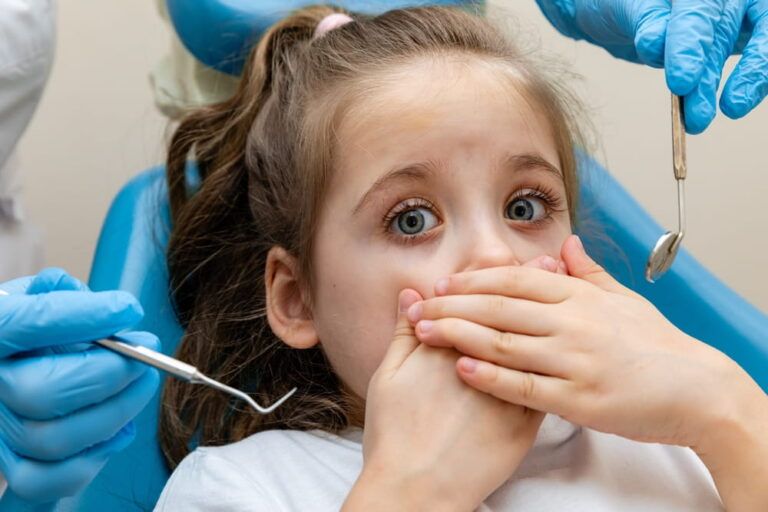 Childish fear. Cute little girl sitting in the dentist chair and covering her mouth in fear