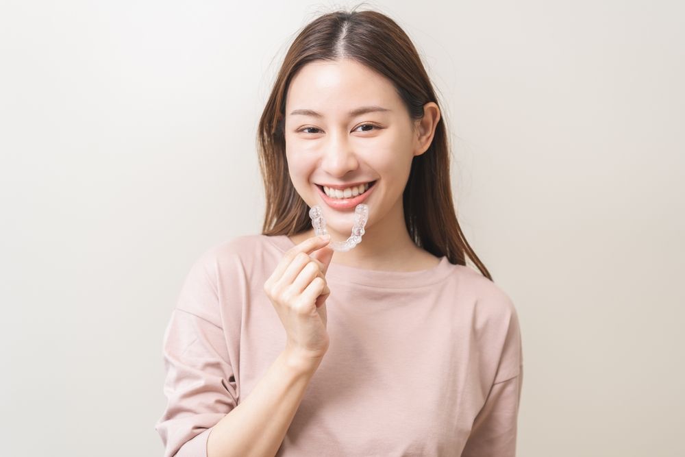 Beautiful smiling young woman holding invisalign braces