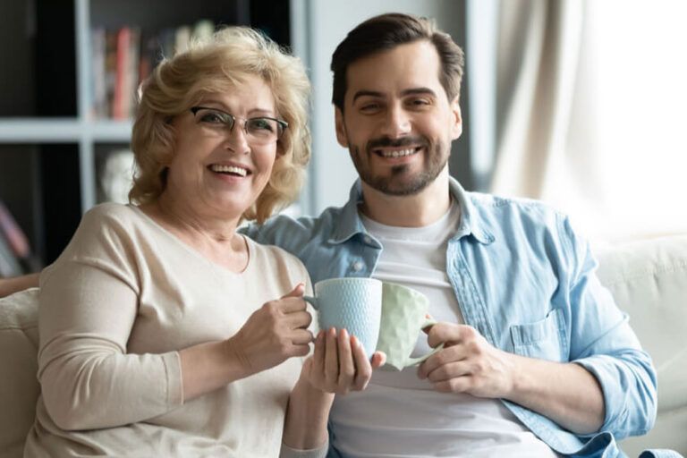 smiling young man and middle-aged mother sit relax on couch
