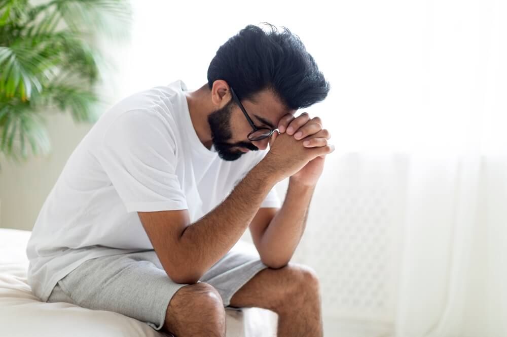 Upset Young Man Sitting On Bed At Home