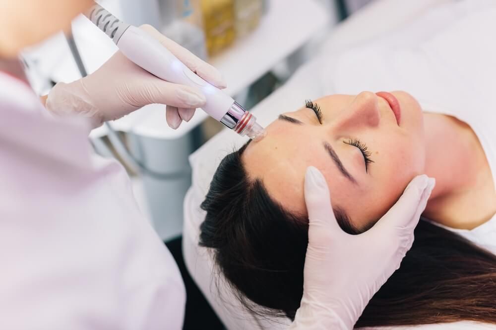 Cosmetologist doing hydrafacial treatment on woman face in beauty clinic