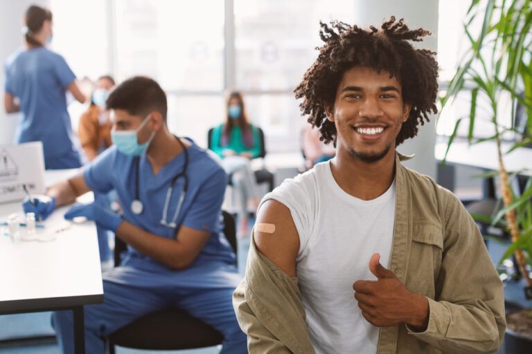 Vaccinated Black Man Gesturing Thumb Up And Showing Arm With Adhesive Bandage After Vaccine Injection