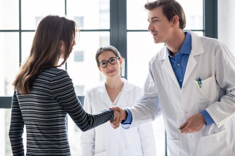 Young dedicated reliable physician and female patient shaking hands before consultation in the office of a modern medical center