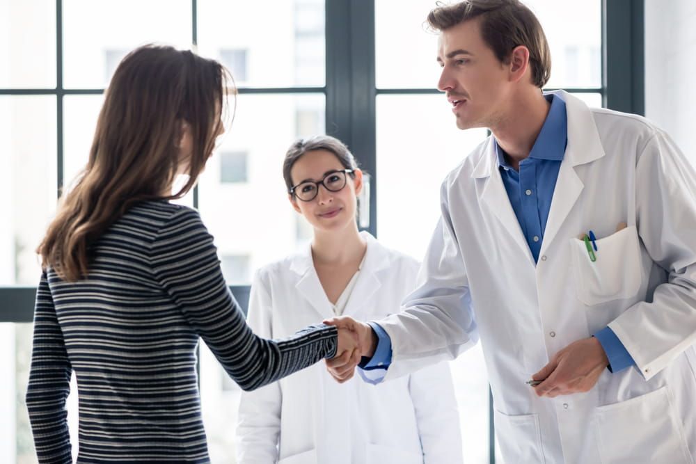 Young dedicated reliable physician and female patient shaking hands before consultation in the office of a modern medical center