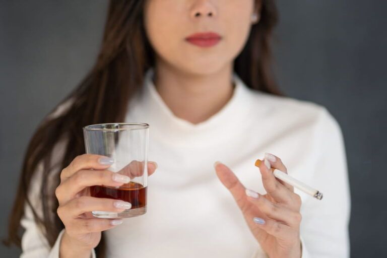 Asian woman hand drinking glass of alcohol and smoking cigarette.