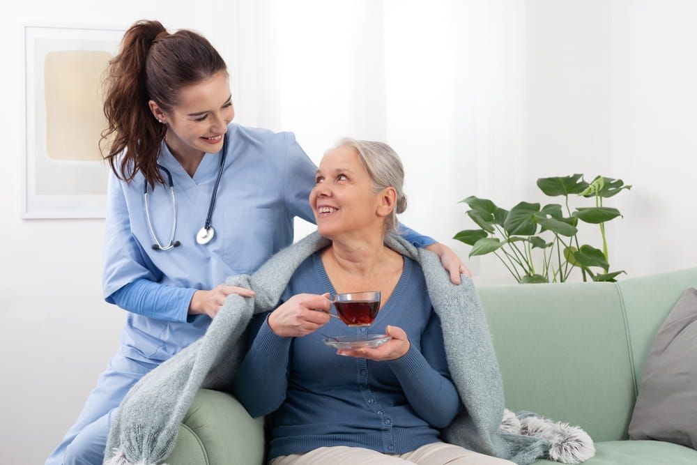 Young woman friendly nurse or doctor caregiver smiles while caring to an elderly senior woman patient.