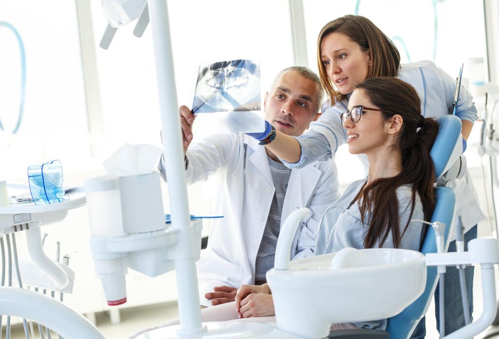 Dentist and his assistant in dental office talking with female patient