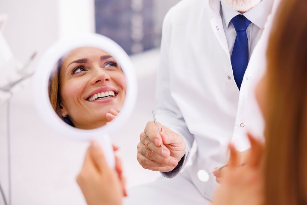 Woman looking in the mirror and smiling after checkup at dentist office