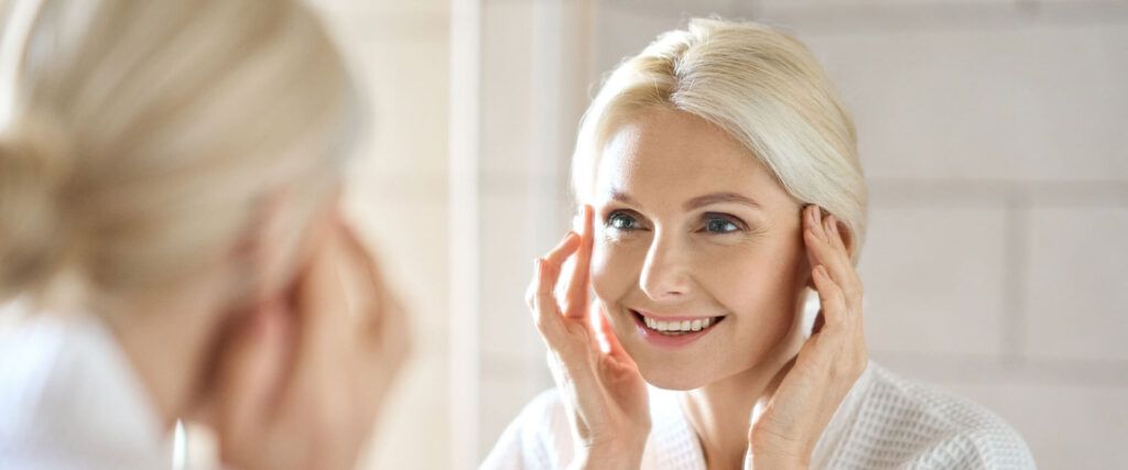 Gorgeous mid age woman looking at reflection in mirror and smiling