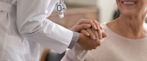 Young female physician leaning forward to smiling elderly lady patient