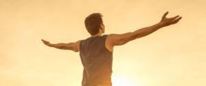 Young man raising his arms up to the sky against the sunset