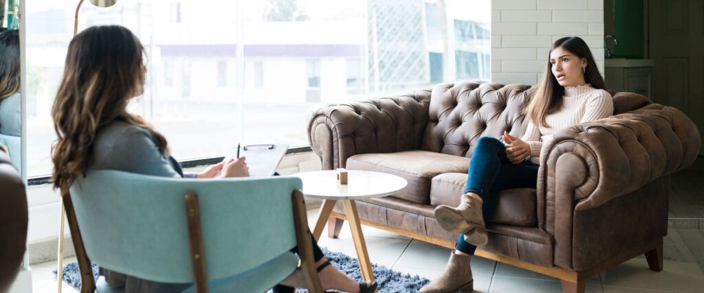 Woman sharing problems with female therapist while sitting on couch at office