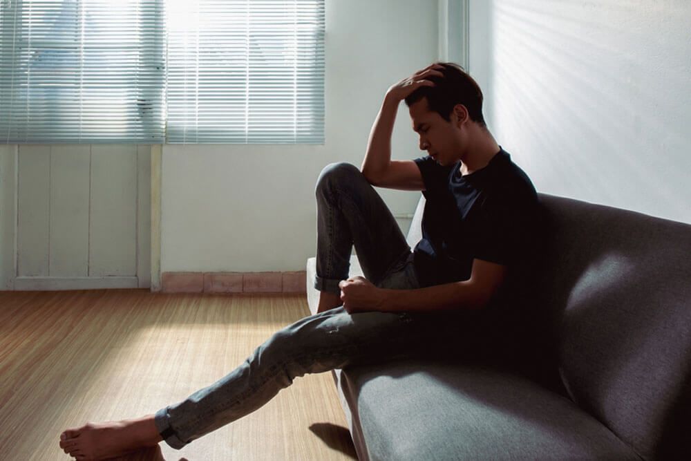 An upset young man sitting alone near a window