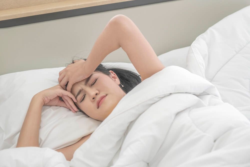 Young woman white lying sheets in a bed with is suffering from headaches