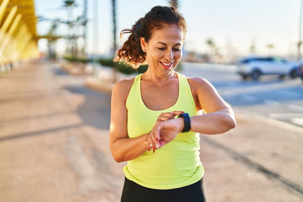 Middle age hispanic woman working out with smart watch at promenade
