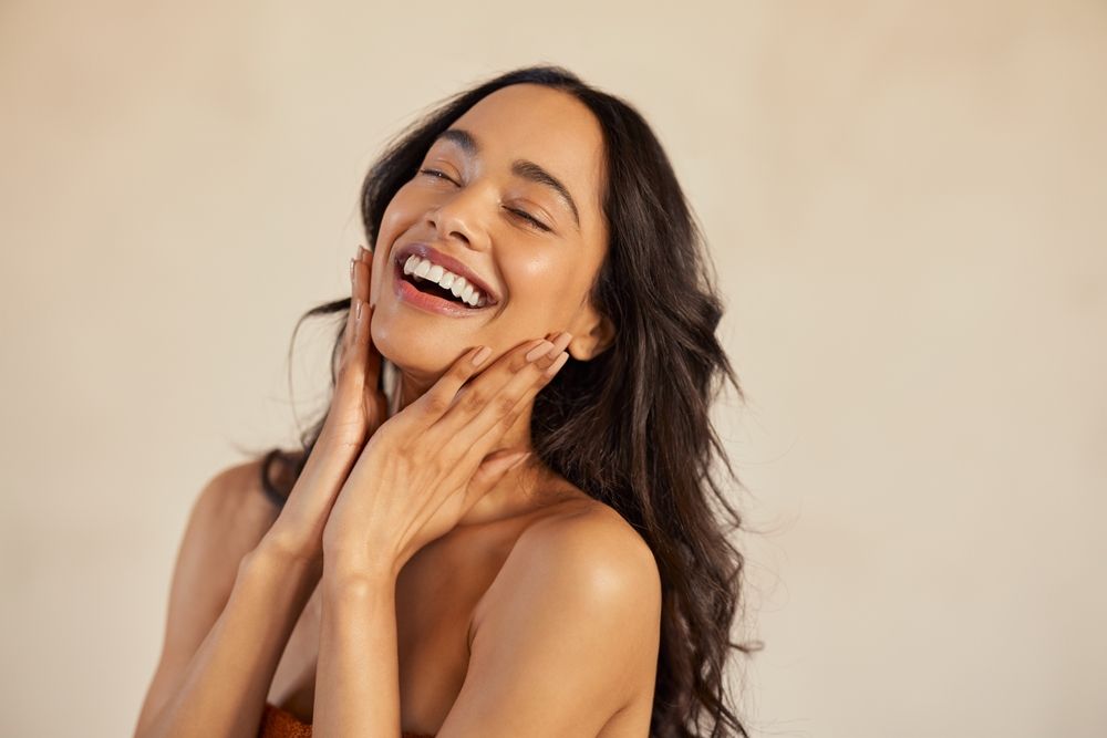 Multiethnic young woman touching her clean and healthy face against background with closed eyes.