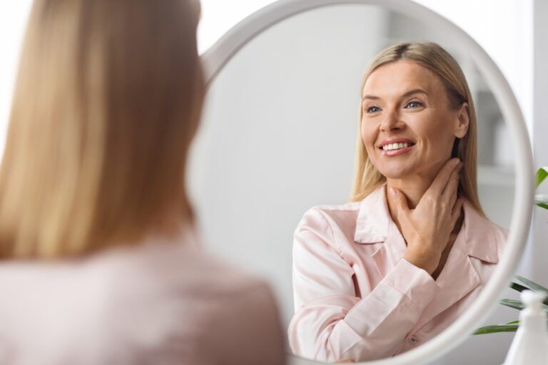 Beautiful Middle Aged Woman Looking At Mirror And Touching Her Soft Skin On Neck