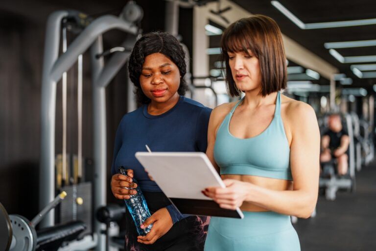 Overweight woman consulting her personal training plan with a fitness instructor in a gym,