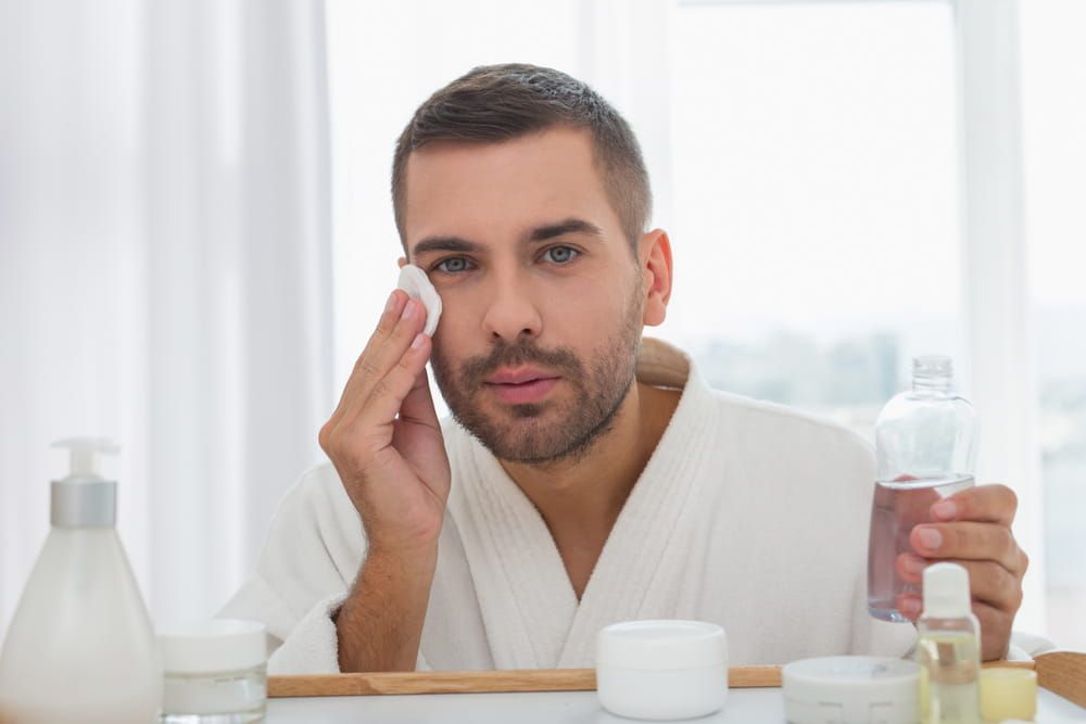 Cleansing lotion. Nice serious man cleaning his skin while using a cleansing lotion