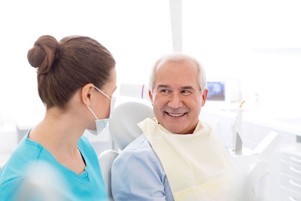 Female dentist talking to smiling senior patient at dental clinic