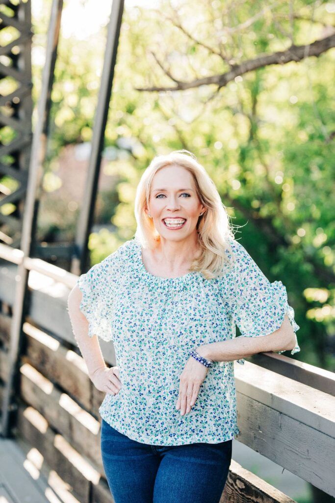 Tammy Frost smiling outdoors leaning on a wooden railing in a natural setting