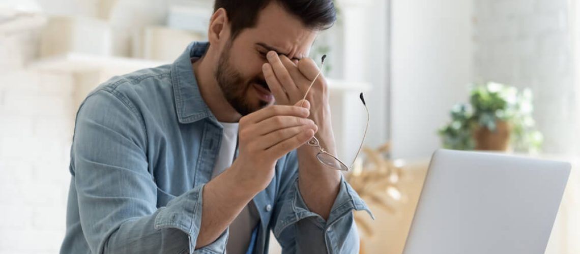 Tired young man feel pain eyestrain holding glasses