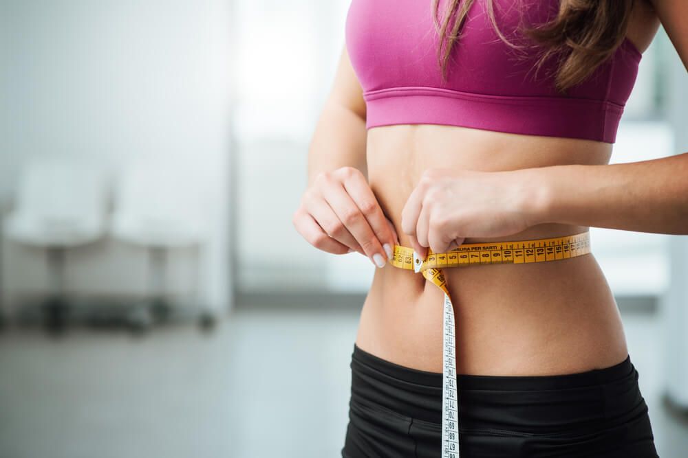 Slim young woman measuring her thin waist