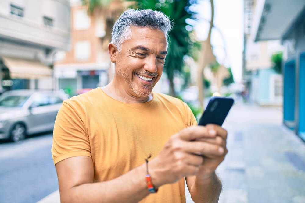 Middle age grey-haired man smiling happy using smartphon