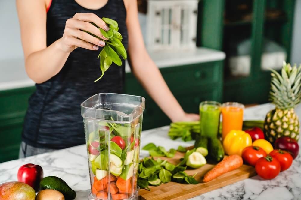 Young girl making green detox cocktail of fresh vegetables and fruits