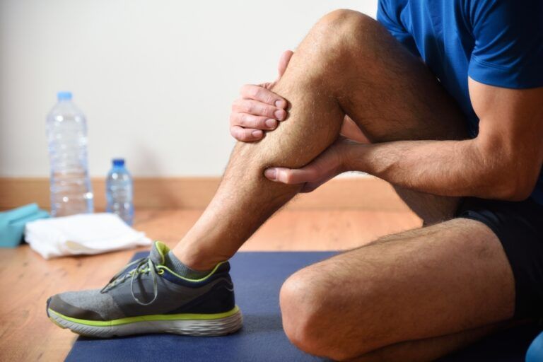 Detail of man doing sports with calf pain holding himself with his hand sitting on a mat. Side view.