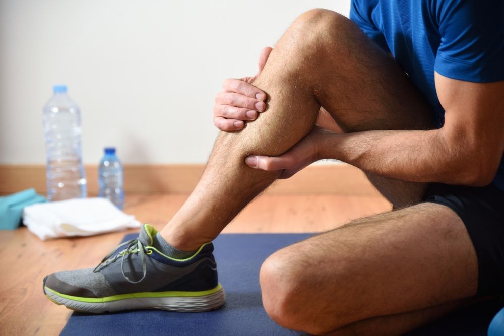 Detail of man doing sports with calf pain holding himself with his hand sitting on a mat. Side view.