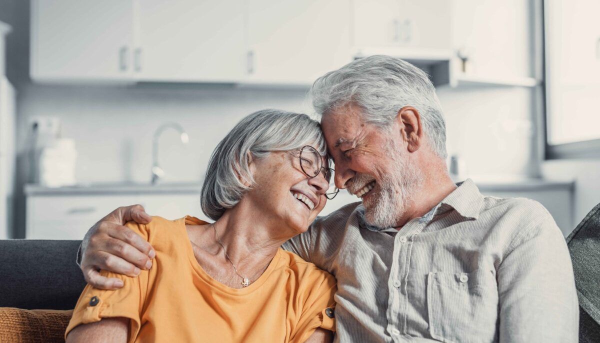 Happy mature husband and wife sit rest on couch at home