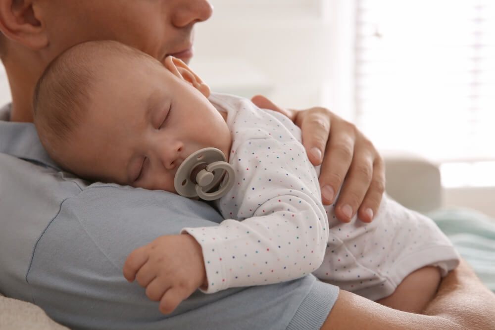 Father holding his cute sleeping baby with pacifier at home