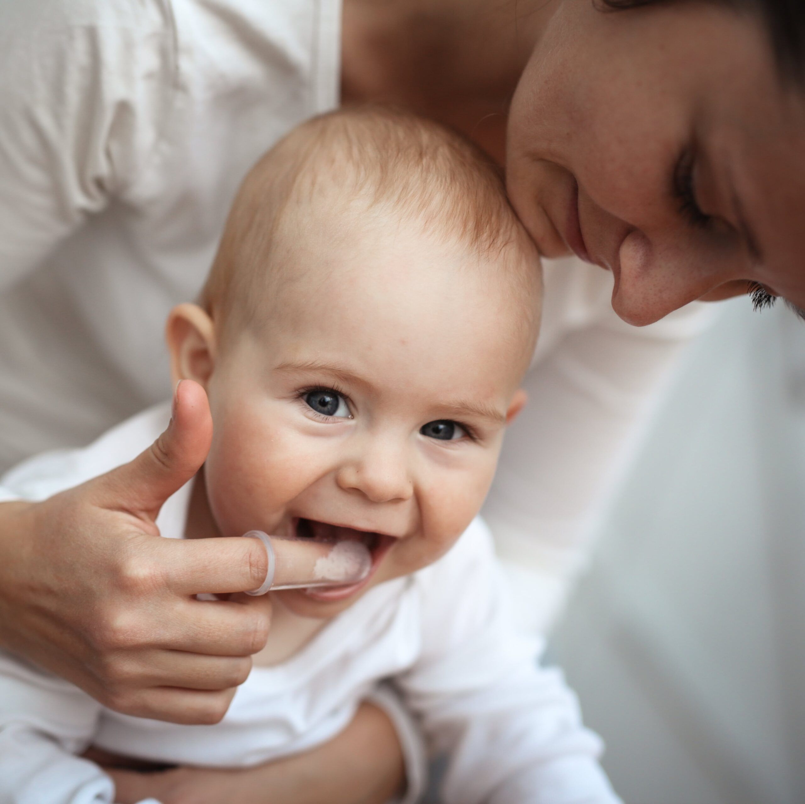 Mom helps to brush the teeth of a happy baby