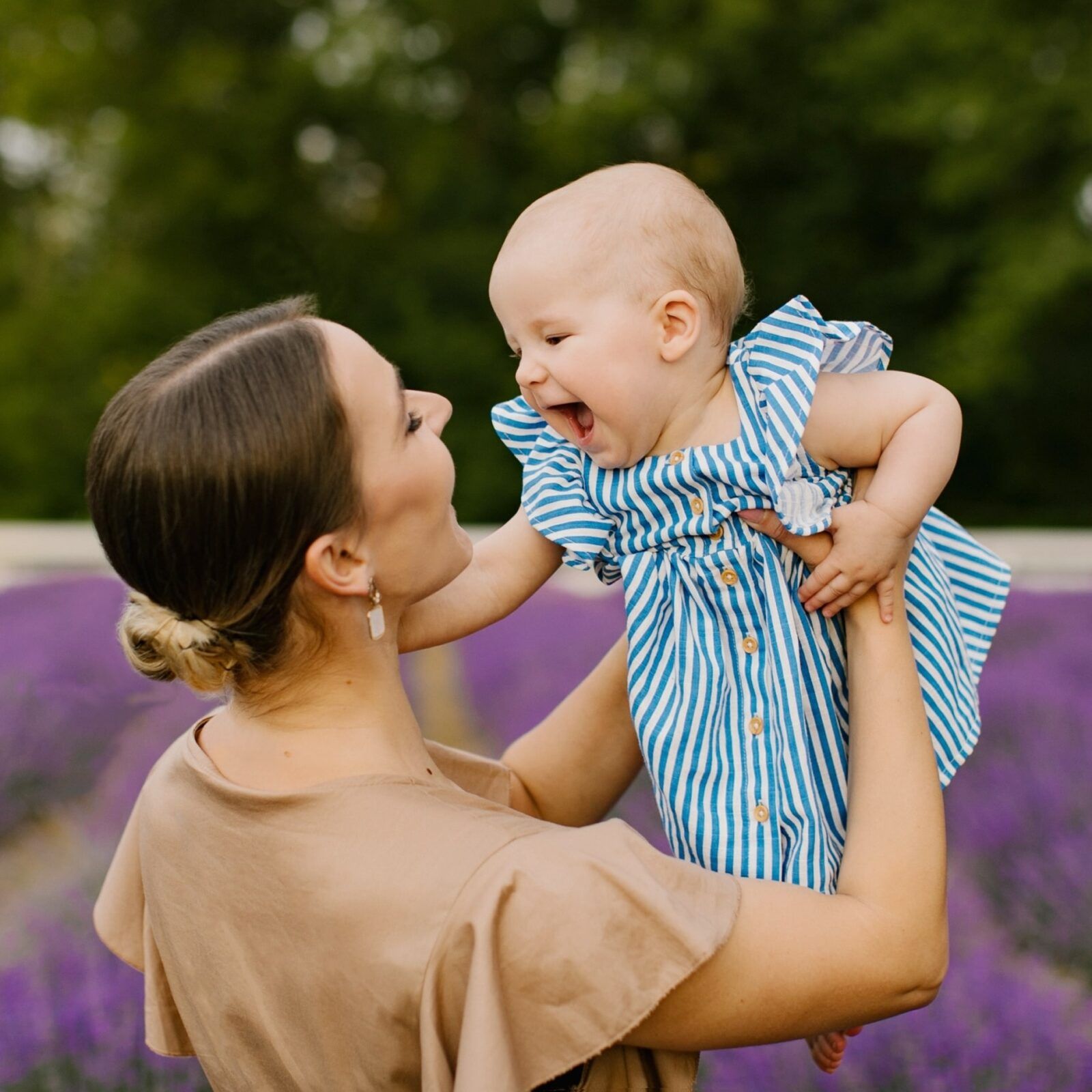 Mom in a brown dress is lifting up her little baby