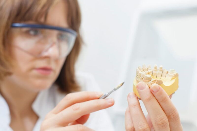 dental technician shaping a prosthesis tooth at work desk