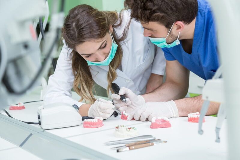 Dental prosthesis, dentures, prosthetics work. Prosthetics hands while working on the denture, false teeth, a study and a table with dental tools.