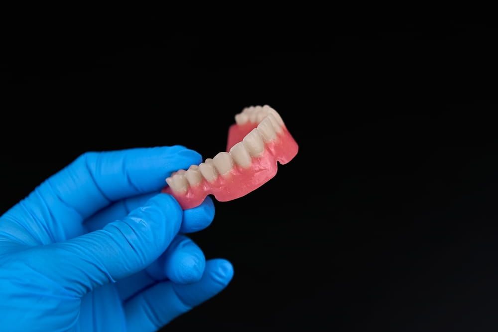 A person has blue gloves on and is holding a denture in their hand