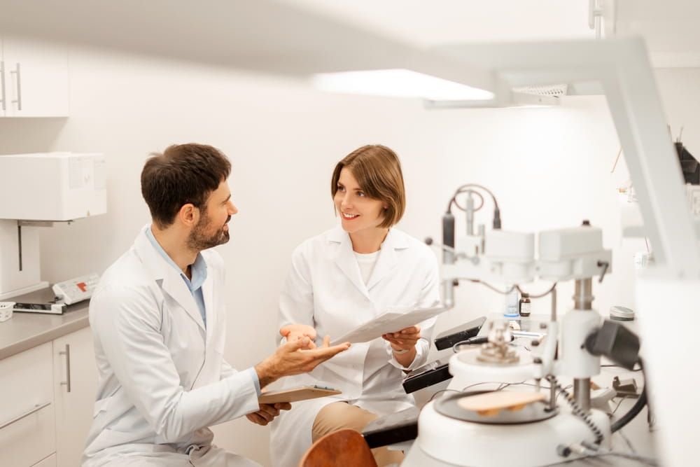 Two dental technicians are discussing a document next to modern milling machine